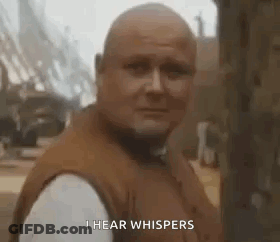 A Bald Man In A Brown Vest Is Standing In Front Of A Tree And Says `` I Hear Whispers '' . GIF