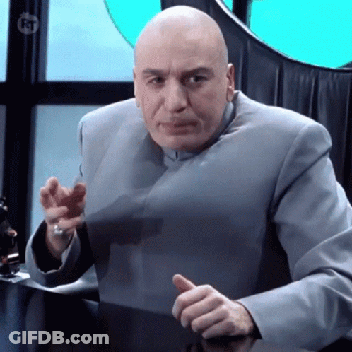 A Bald Man In A Gray Suit Is Sitting At A Desk And Giving A Thumbs Up Sign GIF