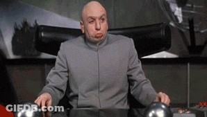 A Bald Man In A Gray Suit Is Sitting At A Desk Making A Funny Face GIF