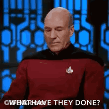 A Bald Man In A Red Shirt Is Sitting In Front Of A Blue Wall And Asking What Have They Done . GIF