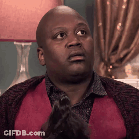 A Bald Man In A Red Vest Is Sitting In Front Of A Lamp And Making A Funny Face . GIF
