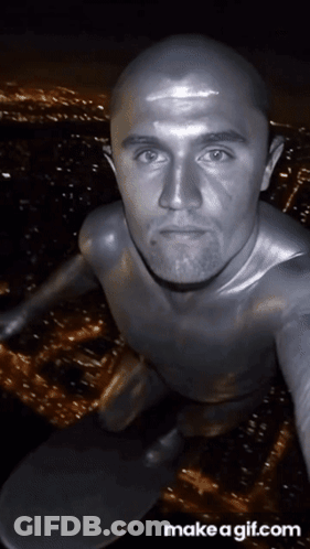 A Bald Man In A Silver Bodysuit Is Taking A Selfie GIF