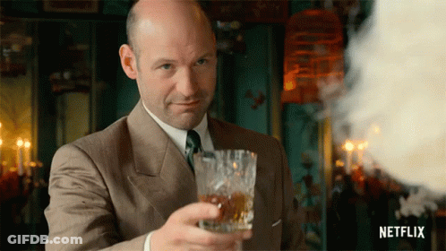 A Bald Man In A Suit And Tie Holds A Glass Of Whiskey GIF