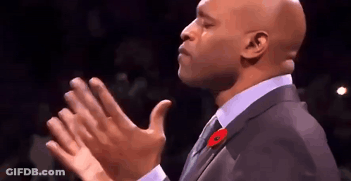A Bald Man In A Suit And Tie Is Clapping His Hands In The Air . GIF