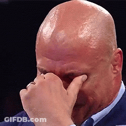 A Bald Man In A Suit And Tie Is Covering His Eyes With His Hand . GIF