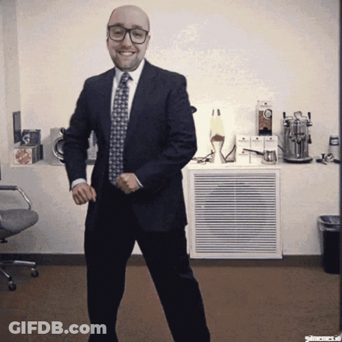 A Bald Man In A Suit And Tie Is Dancing In A Room GIF