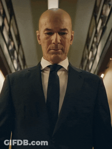 A Bald Man In A Suit And Tie Is Looking At The Camera GIF