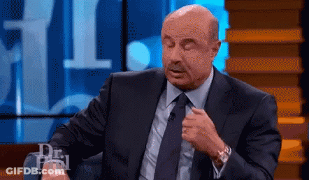 A Bald Man In A Suit And Tie Is Sitting In Front Of A Microphone On A Stage . GIF