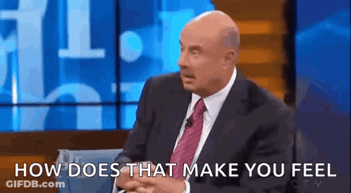 A Bald Man In A Suit And Tie Is Sitting On A Stage And Talking To Someone . GIF