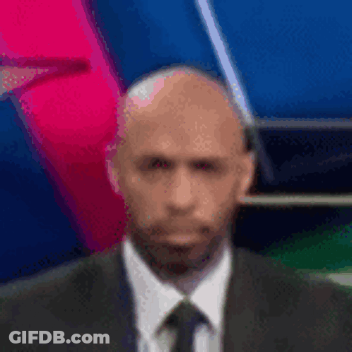A Bald Man In A Suit And Tie Is Standing In Front Of A Colorful Background . GIF