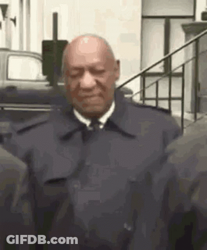 A Bald Man In A Suit And Tie Is Standing Next To A Group Of People . GIF