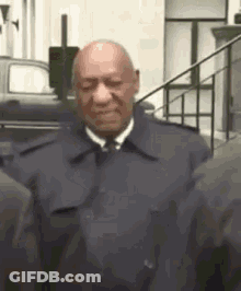 A Bald Man In A Suit And Tie Is Standing Next To A Group Of People . GIF