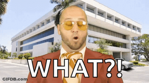 A Bald Man In A Suit And Tie Says What In Front Of A Large Building GIF