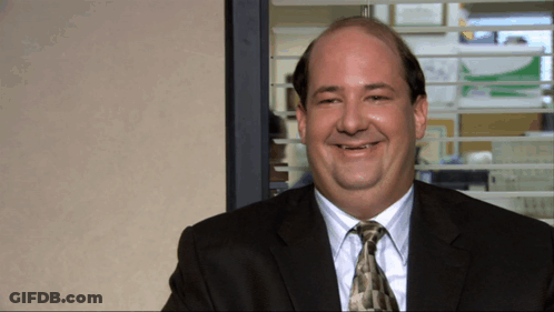 A Bald Man In A Suit And Tie Smiles In Front Of A Window GIF