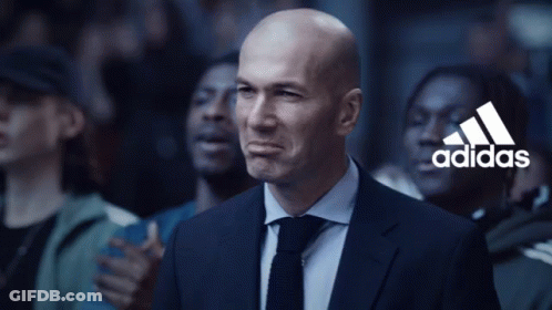 A Bald Man In A Suit And Tie Stands In Front Of A Crowd With The Adidas Logo In The Background GIF
