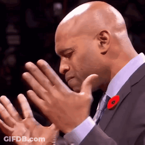 A Bald Man In A Suit And Tie With A Poppy On His Lapel GIF