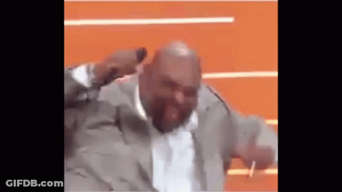 A Bald Man In A Suit Is Dancing On A Stage With His Hands In The Air . GIF