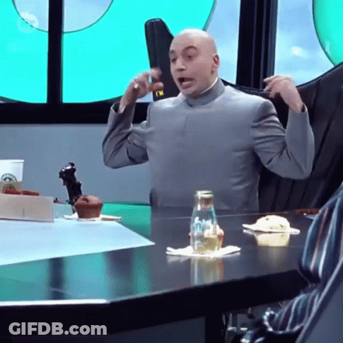 A Bald Man In A Suit Is Sitting At A Table With A Bottle Of Water On It GIF