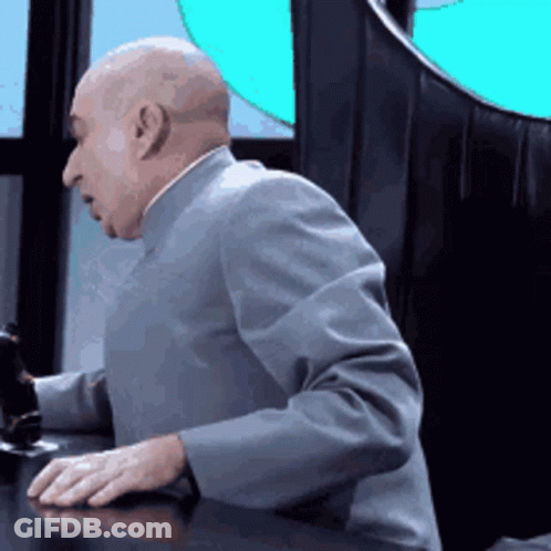 A Bald Man In A Suit Is Sitting At A Table With His Hands On The Desk . GIF