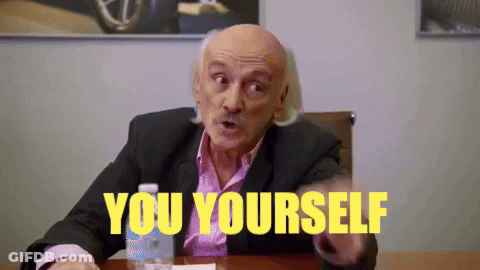A Bald Man In A Suit Is Sitting At A Table With The Words `` You Yourself '' Written In Yellow . GIF