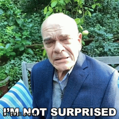 A Bald Man In A Suit Is Sitting On A Bench With The Words I 'M Not Surprised Above Him GIF