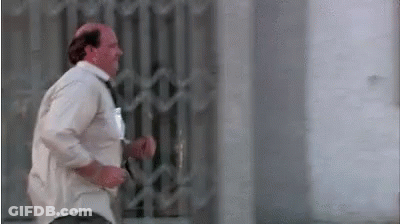 A Bald Man In A White Shirt And Tie Is Running Across A Street . GIF