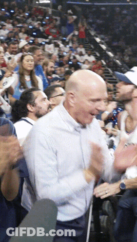 A Bald Man In A White Shirt Is Clapping His Hands In A Crowd GIF