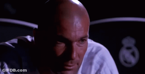 A Bald Man In A White Shirt Is Smiling And Looking At The Camera In A Dark Room . GIF