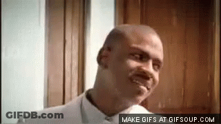 A Bald Man In A White Shirt Is Smiling In Front Of A Door . GIF