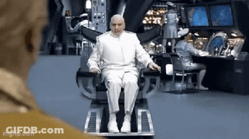 A Bald Man In A White Suit Is Sitting In A Chair In A Room . GIF