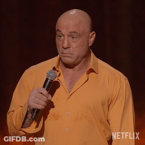 A Bald Man In An Orange Shirt Is Holding A Microphone In Front Of A Netflix Sign GIF
