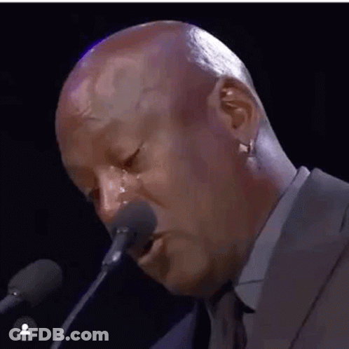 A Bald Man Is Crying While Talking Into A Microphone . GIF