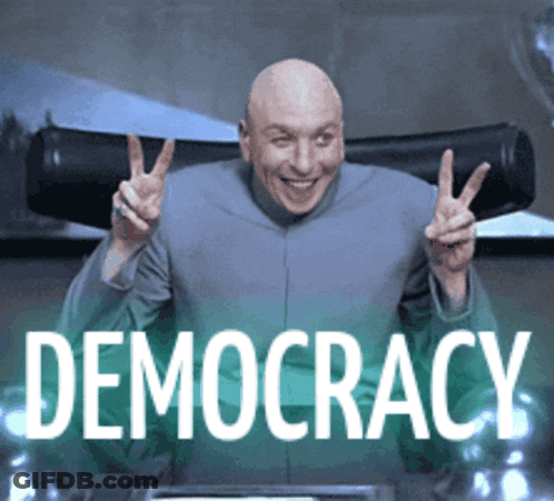 A Bald Man Is Giving A Peace Sign In Front Of A Sign That Says Democracy GIF