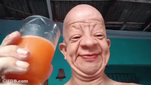 A Bald Man Is Holding A Glass Of Orange Juice And Making A Face . GIF