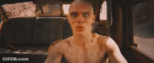 A Bald Man Is Holding A Gun In A Car With Flames Coming Out Of The Back Seat . GIF