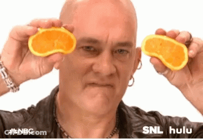 A Bald Man Is Holding Two Orange Slices In Front Of His Eyes . GIF