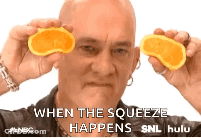 A Bald Man Is Holding Two Slices Of Orange In Front Of His Eyes And Says When The Squeeze Happens . GIF