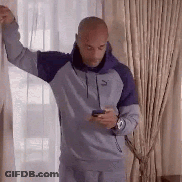 A Bald Man Is Leaning Against A Wall While Looking At His Phone . GIF