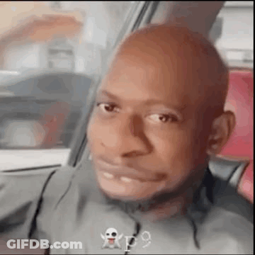 A Bald Man Is Making A Funny Face While Sitting In The Back Seat Of A Car . GIF