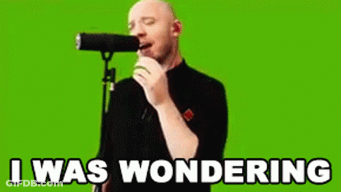 A Bald Man Is Singing Into A Microphone With The Words `` I Was Wondering '' Written On The Screen Behind Him . GIF