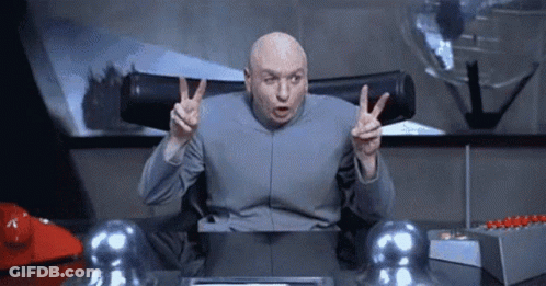 A Bald Man Is Sitting At A Desk And Giving A Peace Sign . GIF