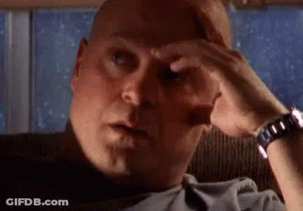 A Bald Man Is Sitting In A Chair With His Hand On His Forehead And A Watch On His Wrist . GIF