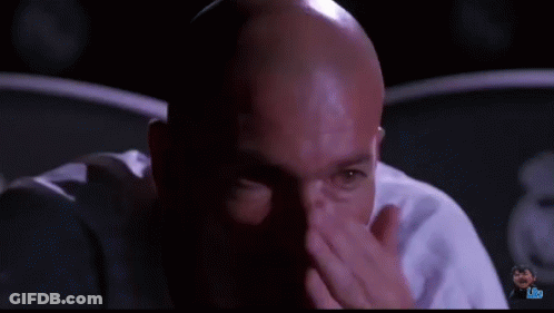 A Bald Man Is Sitting In A Dark Room And Looking At The Camera GIF