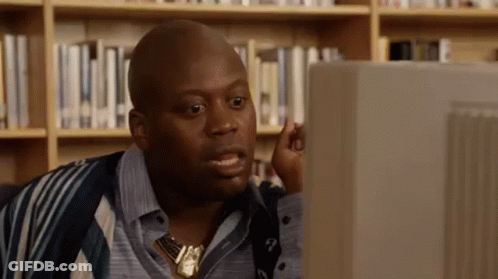 A Bald Man Is Sitting In Front Of A Computer Screen In A Library . GIF