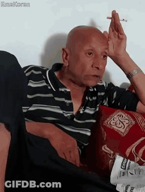 A Bald Man Is Smoking A Cigarette While Sitting On A Couch GIF