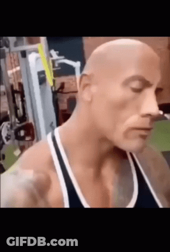A Bald Man Is Standing In A Gym With His Eyes Closed And A Black Tank Top On . GIF