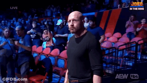 A Bald Man Is Standing In Front Of A Crowd In A Wrestling Ring . GIF