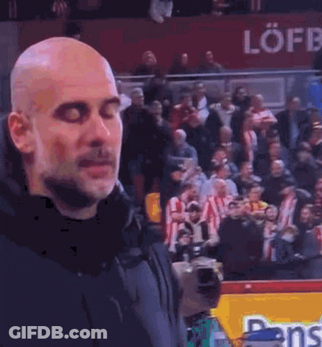 A Bald Man Is Standing In Front Of A Crowd Of People Watching A Soccer Game . GIF