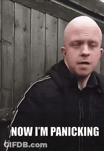 A Bald Man Says " Now I 'M Panicking " In Front Of A Wooden Wall GIF