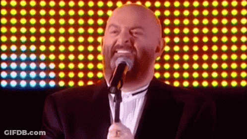 A Bald Man Singing Into A Microphone With A Beard GIF